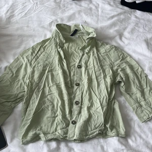 Ljusgrön skjorta från Divided, strl 36 - Snygg ljusgrön skjorta från Divided i storlek 36. Skjortan har klassisk krage, knäppning framtill med fyra knappar och långa ärmar. Tillverkad i mjuk bomull, perfekt för en chill och stilren look.