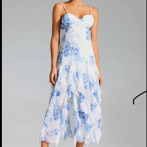 klänning - Superfin vit långklänning med blå  blommor, tunna axelband och öppen rygg. Klänningen har volangdetaljer och är perfekt för sommarens alla tillfällen ❤️. Tyvärr var den lite för stor på mig och är helt oanvänd. (Sista bilden är inte min, utan vill visa hur den sitter på någon annan🥰)