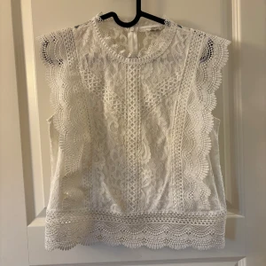 Spetsblus - Superfin vit blus från ONLY med detaljerad spets och blommigt mönster. Perfekt för dig som gillar romantisk och feminin stil. Dragkedja bak för enkel påklädning.