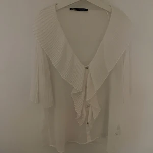 Vit volang blus zara - Jätte fin oanvänd blus från zara! Tunt material perfekt för sommaren när det lite varmare. Vita blus med lite volanger i mitten. Super gullig och söt! 