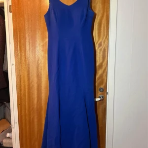 Blå långklänning med v-ringning - Säljer en elegant blå långklänning med v-ringad halsringning. Klänningen har en figurnära passform upptill och faller snyggt längs kroppen. Perfekt för bal eller festliga tillfällen.