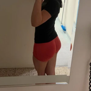 Röda träningsshorts - Säljer ett par röda tighta träningsshorts med korta ben och elastisk midja. Perfekta för gymmet eller löpning, sitter skönt och framhäver formen. Materialet är stretchigt och andas bra. Snygg och enkel design utan mönster eller detaljer.