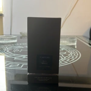 Tom Ford Oud Wood EdP 100ml - Tom Ford Oud Wood Eau de Parfum 100 ml säljes. Flaskan är mörkbrun med elegant, fyrkantig design och tillhörande kartong i samma färg. Doften är känd för sina träiga och lyxiga oud-noter. Perfekt för dig som gillar exklusiva och djupa parfymer.