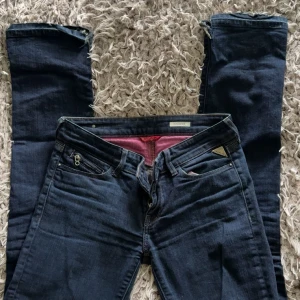 Mörkblå Replay jeans med dragkedjedetalj - Snygga mörkblå jeans från Replay med dragkedjedetalj på fickan och broderad logga. Klassisk femficksmodell i stretchigt jeanstyg. Passar dig som gillar en stilren look med lite edge.