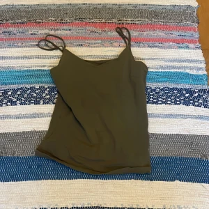Olivgrön linnetopp med smala axelband - Snygg olivgrön linnetopp med smala axelband och enkel, stilren design. Perfekt att matcha med jeans eller kjol för en avslappnad look. Tunt och mjukt material som känns skönt mot huden.