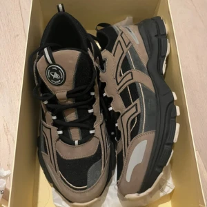 Axel Arigato Marathon Runner sneakers - Chunky sneakers från Axel Arigato i modellen Marathon Runner. Skorna har en beige och svart färgkombination med detaljer i grått och vitt. Ovandelen är i mocka och mesh, med svarta snören och en kraftig svart sula. Perfekta för dig som gillar streetstyle och statement-sneakers.