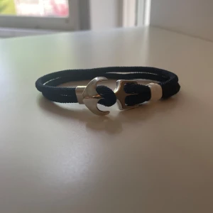 Ankar armband - Stilrent armband med svart rep och ett silverfärgat ankare som lås. Perfekt accessoar för en marin inspirerad look. Ankaret ger en unik detalj och armbandet är lätt att bära till olika outfits. Skriv till mig vid minsta lilla fundering!