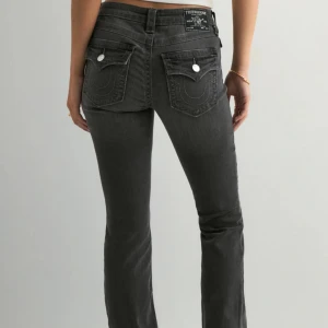 Svarta jeansbyxor från True Religion - Snygga svarta jeansbyxor från True Religion med klassiska bakfickor och vita knappar. Byxorna har normal passform och raka ben, perfekt till vardags. Tydlig logga på bakre linningen och detaljerade sömmar på fickorna. Helt nya