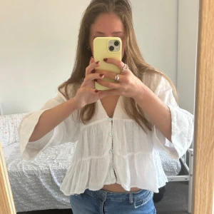 Vit blus med knappar - Säljer en luftig vit blus med v-ringning och knappar framtill. Blusen har trekvartsärmar och volangdetaljer, perfekt för varma dagar. Passar snyggt till jeans eller kjol.