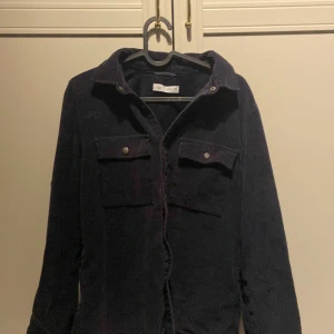 Svart manchester overshirt med fickor - Snygg marinblå overshirt i manchester med två stora bröstfickor och coola metallknappar. Perfekt att slänga över en hoodie eller t-shirt för en chill look. Långärmad och med klassisk krage.