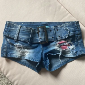 Blå jeansshorts med bälte från Amule - Snygga blå jeansshorts från Amule med tillhörande brett bälte och slitna detaljer framtill. 