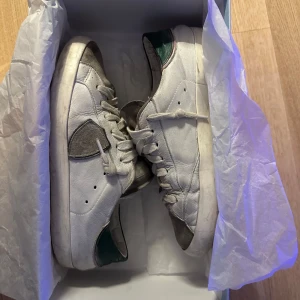 Phillip model - Säljer ett par vita Philippe Model sneakers med gråa och gröna detaljer. Skorna har snörning, rund tå och platt sula. Klassisk design med logotyp på sulan och bekväm passform. Perfekta för dig som gillar stilrena och sportiga skor. ÄR 36 MEN PASSAR 100% SOM 37-37,5. PRISET GÅR ATT DISKUTERA!