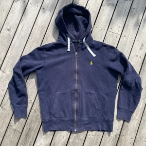 Marinblå hoodie från Polo Ralph Lauren - Säljer en riktigt snygg marinblå hoodie från Polo Ralph Lauren med dragkedja och vit logga på bröstet. Perfekt för en avslappnad stil. Storleken är m men den sitter som s