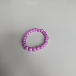 Lila pärlarmband med marmoreffekt - Snyggt armband med runda lila pärlor och marmorerad effekt. Elastiskt band gör det enkelt att ta på och av. Perfekt accessoar för att addera lite färg till din outfit.