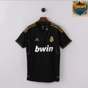 Real Madrid svart bortatröja Adidas - Svart Real Madrid bortatröja från Adidas med guldiga detaljer och tre ränder på axlarna. Tryckt Bwin-logga på bröstet och broderat klubbmärke. Tillverkad i lätt och ventilerande funktionsmaterial, perfekt för fotboll eller supporterliv.