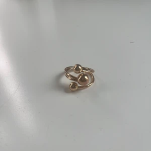 guldig ring med kulor - Cool och modern ring i guldton med tre blanka kulor i olika storlekar. Ringen har en öppen, snirklig design som ger en unik och edgy look. Perfekt för dig som vill ha en super gullig vardaglig ring! Justerbar och säljer då den inte kommer till användning! Skriv om ni har frågor! 