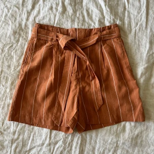 Randiga shorts med knytband - Snygga shorts med vita ränder och knytband i midjan. Shortsen har hög midja, bälteshällor och fickor både fram och bak. Knappt använda så i väldigt fint skick. 
