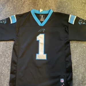 Carolina Panthers Newton NFL tröja - 📸 Strl: M/L (normal passform – oversized för S) (Liten i form) 🏈 Svart Cam Newton #1 Carolina Panthers NFL-tröja 💙 Snygga blå detaljer, meshpaneler – klassisk jersey-look 🇺🇸 Import från USA – inte lätt att hitta i Sverige  🎯 För dig som älskar amerikansk fotboll, streetwear eller bara vill ha en clean svart tröja med edge.  💡 Sitter snyggt både som t-shirt och över hoodie – perfekt till vardag, sommarhäng eller festival. 📸 Använd 1–2 gånger, i mycket fint skick!  💸 Prisidé: 450 kr (öppen för bud)