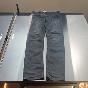 Levi's 512 svarta jeans slim taper - Svarta Levi's 512 jeans med slim taper passform. Klassisk femficksdesign, bälteshällor och dragkedjegylf. Jeansen är i bomullsmix och har en något tvättad look för en avslappnad vibe. Perfekta för dig som gillar en smalare siluett men ändå vill ha lite utrymme vid benen.