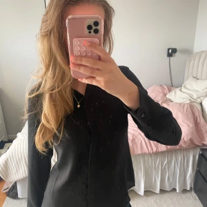 Svart skjorta med knappar - Snygg svart skjorta med klassisk krage och knäppning framtill. Långärmad modell som passar perfekt till många olika outfits. Enkel och stilren design som är lätt att matcha.