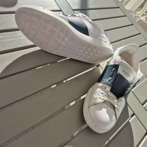 Vita/Mörkgröna Valentino Open skor - Säljer ett par vita/Mörkgröna sneakers från Valentino Garavani😁 De har en bred mörkgrön panel på sidan med ikoniska nitar längs bakre sulan✅️. Skorna har snörning och rund tå, tillverkade i skinn🤩. Perfekta för dig som gillar stilrena och exklusiva sneakers👍😉. Inga stora defekter förutom slitmärket vid sidan på de mörkgröna. Säljer dessa för endast 1199kr då nypriset på dessa är 7000kr+. Priset kan alltid diskuteras😁👍 Ingen originalbox förs tyvärr med!
