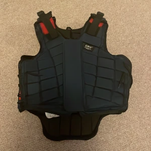 Mörkblå ridväst från CRW - jag säljer en mörkblå ridväst ifrån märket CRW, västen är bara anbänd några gånger och är i nyskick, ridvästen är för 8 årkngar men den är justerbar!