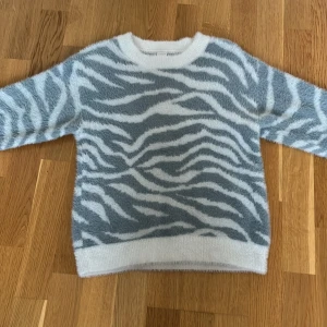 Fluffig zebramönstrad tröja - Supermjuk och fluffig tröja med zebramönster i ljusgrått och vitt! Tröjan är ifrån Lindex men säljs inte längre. Den är i storlek 134/140 men den är stor i storleken så den sitter som xs/s. Säljer på grund av att den är för liten i ärmarna!❣️