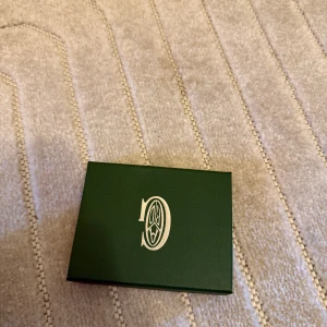  Grå korthållare i skinn - Säljer en stilren grå korthållare  med deras ikoniska mönster. Korthållaren har flera fack för kort och är tillverkad i skinn med snygga detaljer. Perfekt för dig som vill ha något exklusivt och smidigt i fickan.