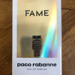 Fame Eau de Parfum från Paco Rabanne - Säljer en lyxig parfym, Fame Eau de Parfum från Paco Rabanne. Förpackningen är vit med holografisk framsida och en ikonisk robotfigur. Parfymen är vegansk, tillverkad i Frankrike och har en långvarig doft.