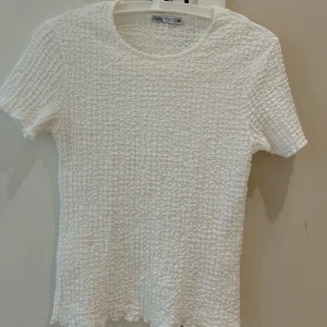 Vit topp från Zara - Säljer en vit  topp från Zara med korta ärmar och rund halsringning. Toppen har en strukturerad, lite bouclé-liknande yta som ger en unik känsla. Perfekt att styla till olika outfits!