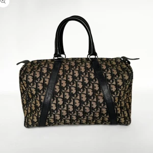 Dior väska  - Säljer en klassisk handväska från Dior med ikoniskt monogrammönster i brunt och svart. Väskan har svarta handtag och detaljer i skinn samt dragkedja upptill. Perfekt för dig som vill ha en tidlös och snygg accessoar.