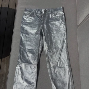 Silvriga jeansbyxor från Gina tricot - Säljer ett par riktigt silvriga jeansbyxor från Gina tricot. Byxorna har klassisk femficksdesign, normal passform och är tillverkade i ett glansigt material. Storlek 38, inte mkt stretch