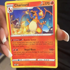Charizard Pokémonkort - Säljer ett Charizard Pokémonkort med 170 HP från Sword & Shield-serien. Kortet har en färgstark illustration av Charizard med eld i bakgrunden och innehåller attackerna Battle Sense och Royal Blaze. Perfekt för samlare eller Pokémon-fans.
