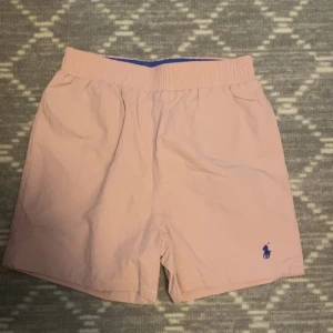 Ljusrosa shorts från Polo Ralph Lauren - Snygga ljusrosa shorts från Polo Ralph Lauren med elastisk midja och klassisk broderad logga i blått på benet. Perfekta för sommardagar och har en enkel, stilren design. Köpt för 2000, mitt pris 599kr