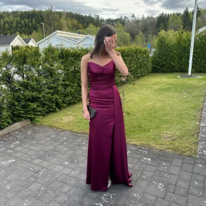 Vinröd långklänning med slits  - Säljer denna jätte fina balklänning då jag köpte en annan jag ska ha på min bal å vill inte låta denna gå till spillo, helt ny aldrig använd prislapp är kvar, har köpt klänning utomlands❤️hög kvalité och sitter extremt bra, har som en korsett på överkroppen vilket gör att den hålls på plats och är där med perfekt för lite mindre byst🌷❤️jag är 178+ låg kitenhil å den går hela vägen❤️❤️nypris på klänningen låg på 2000kr🌷