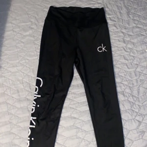 Svarta leggings från Calvin Klein - Svarta leggings från Calvin Klein med hög midja och vita logotyper längs benet och vid höften. Stretchigt material som sitter tight och bekvämt. Perfekta för både träning och chill.