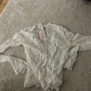 Vit spetsblus från Nelly - Säljer en superfin vit blus i spets från Nelly. Blusen har långa ärmar och vackra spetsdetaljer över hela plagget. Perfekt för dig som vill ha en romantisk och feminin look.