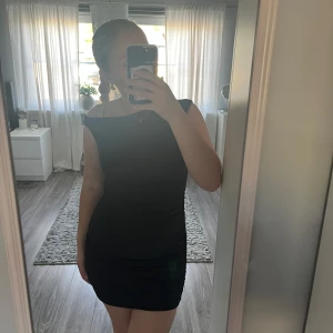 Svart tight kortklänning - Säljer en svart tight kortklänning med breda axelband och rund halsringning. Klänningen har en enkel och stilren design som passar perfekt till olika tillfällen. Bekväm passform och smickrande siluett. Aldrig använd