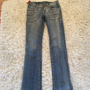Blå jeansbyxor från Miss Vivi Collection - Säljer ett par blå jeansbyxor från Miss Vivi Collection med slitna detaljer och utsvöngda ben. Byxorna har fram- och bakfickor, bälteshällor och dekorativa sömmar. Snygg tvätt och klassisk femficksmodell.