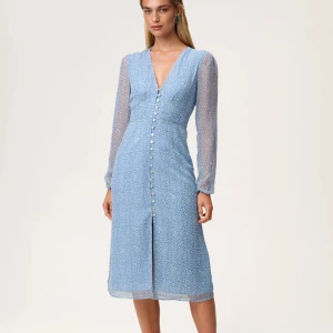 Ljusblå klänning med knappar och lång ärm - Säljer en ljusblå klänning med v-ringning, långa transparenta ärmar och knappar framtill. Klänning är aldrig använd och har prislappen på sig!