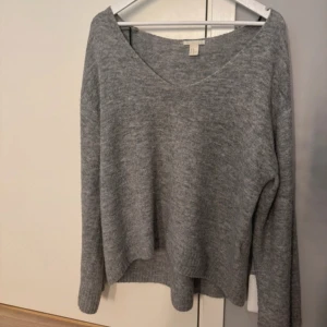 Grå stickad tröja från H&M - Grå stickad tröja från H&M med v-ringad hals och lång ärm.  Använd men fortfarande mycket gott skick. Lite oversized 