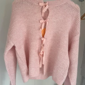 Rosa stickad kofta med rosetter - Säljer helt oanvänd superfin rosa stickad kofta med unika rosettdetaljer, eftersom att den aldrig har kommit till användning. . Mjuk och mysig modell med lång ärm och avslappnad passform. Perfekt för dig som vill ha något gulligt och annorlunda i garderoben!