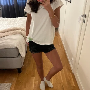 Svarta jeansshorts med fransar och slitningar - Snygga svarta jeansshorts med råa fransar i benslut och slitna detaljer framtill. Klassisk femficksmodell med knapp och dragkedja. Perfekta för sommaren och ger en cool, avslappnad look.