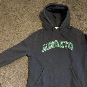 Mörkblå hoodie från Arigato - Säljer en mörkblå hoodie från Arigato med grön och vit text på bröstet. Storlek Small, bra skick. Mitt pris 399kr