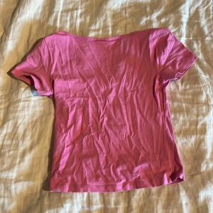 Rosa t-shirt med djup urringning - En enkel rosa t-shirt med korta ärmar och djup rund urringning. T-shirten är i mjukt material och har en klassisk passform som passar till många olika stilar. Man kan ha den från och bak.