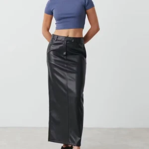 Svart långkjol i skinnimitation - Säljer en svart långkjol i skinnimitation från Ginatricot. Kjolen har hög midja, bälteshällor och en diskret slits baktill. Snygg och stilren modell som passar perfekt till många olika looks.