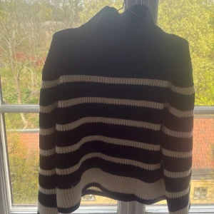 Svartvit randig stickad polotröja från Gina Tricot - Säljer en svart och vit stickad polotröja från Gina Tricot. Tröjan har breda horisontella ränder, hög krage och långa ärmar. Perfekt för dig som gillar en klassisk och mysig stil.