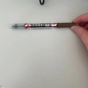 Build-A-Brow  - Ögonbrynspenna från Maybelline i nyansen 255 Soft Brown. Pennan har en borste i ena änden för att forma och sudda ut färgen. Perfekt för att fylla i och definiera brynen med ett naturligt resultat.