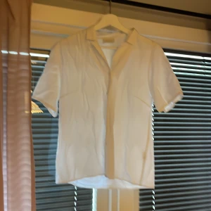 Vit kortärmad skjorta från Choise - Säljer en klassisk vit skjorta från Choise med korta ärmar och krage. Skjortan har en rak passform och är tillverkad i ett lätt och svalt material, perfekt för varmare dagar. Enkel och stilren design som passar till många tillfällen.