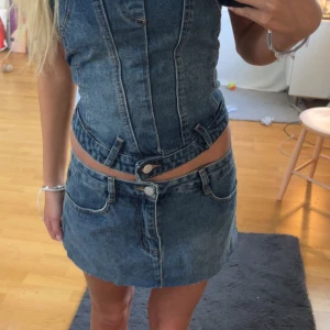 Jeanskjol med låg midja - Säljer en kort jeanskjol i klassisk blå denim med låg midja och synliga sömmar. Kjolen har fickor fram och knäppning med knapp och dragkedja. Perfekt för dig som gillar en trendig och avslappnad stil.